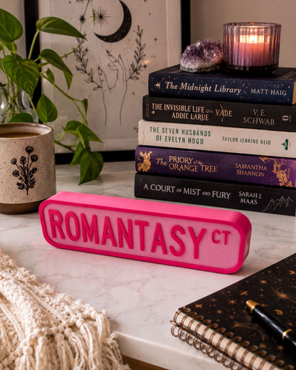 a collection of books, a pink object, and some decorative elements arranged on a white marble surface.