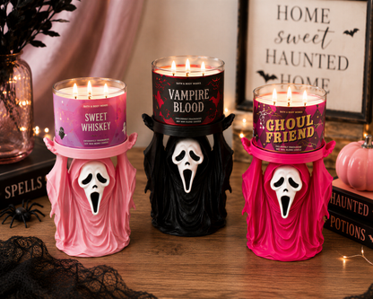 three Halloween-themed candles with spooky faces, placed on a wooden surface.