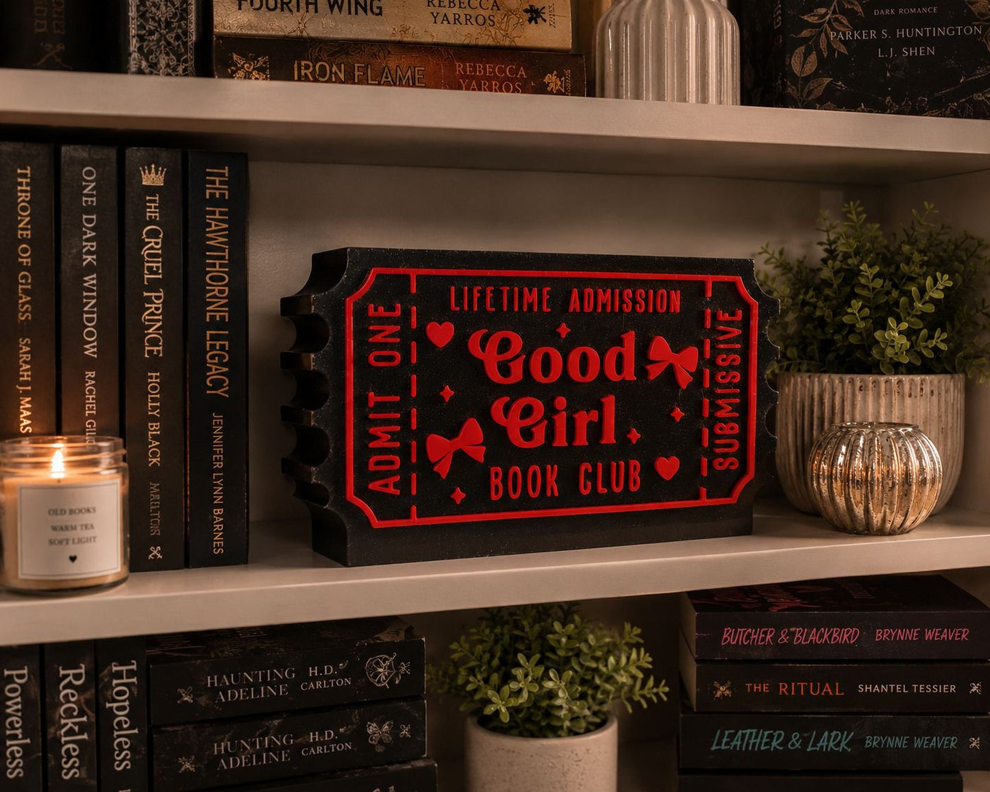 a bookshelf with various books, a candle, and decorative items such as a potted plant and a vase.