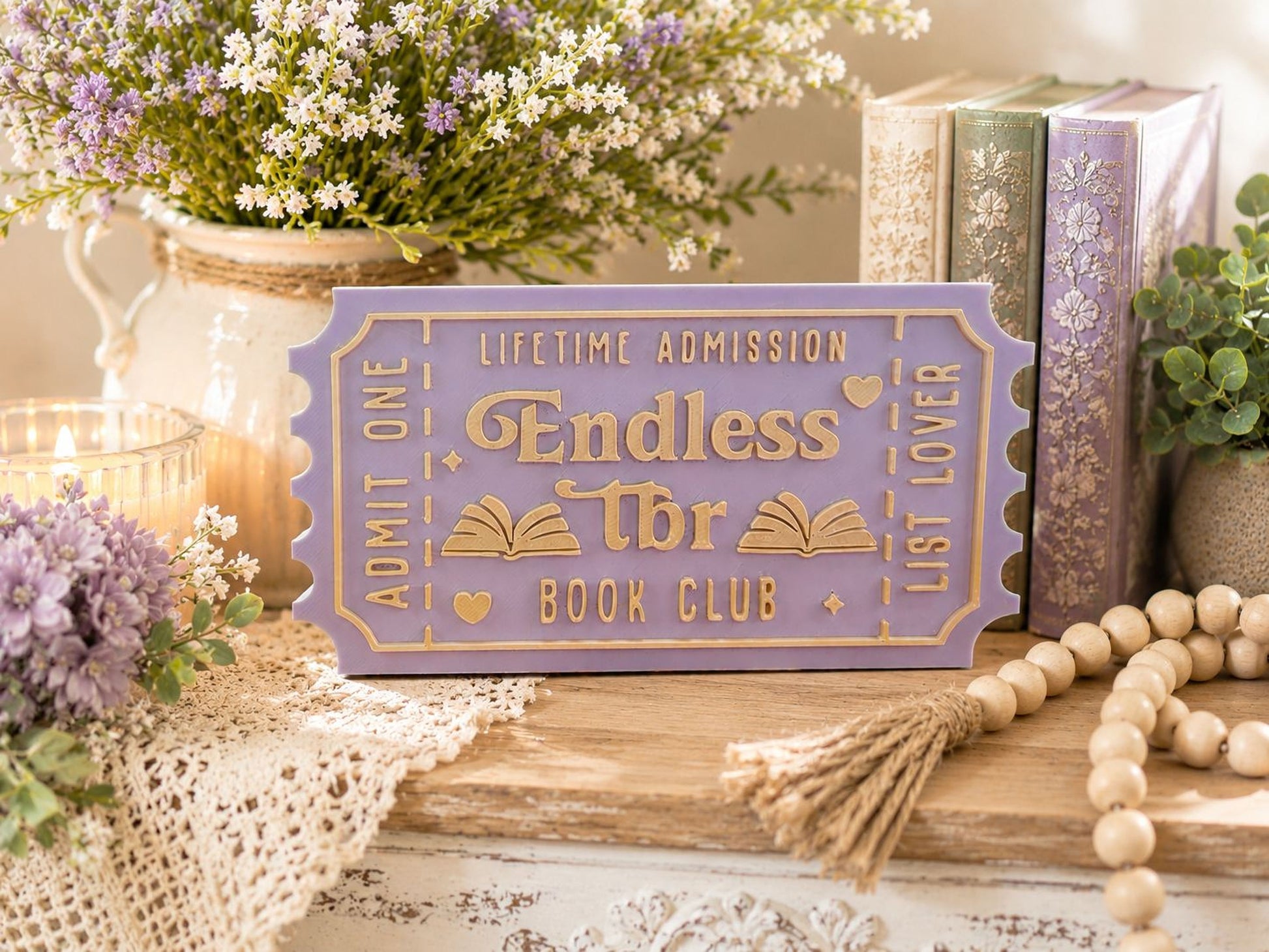 a purple ticket-shaped sign with the words "Endless" and "Book Club" on it, surrounded by various decorative items such as books, flowers, and a beaded string.