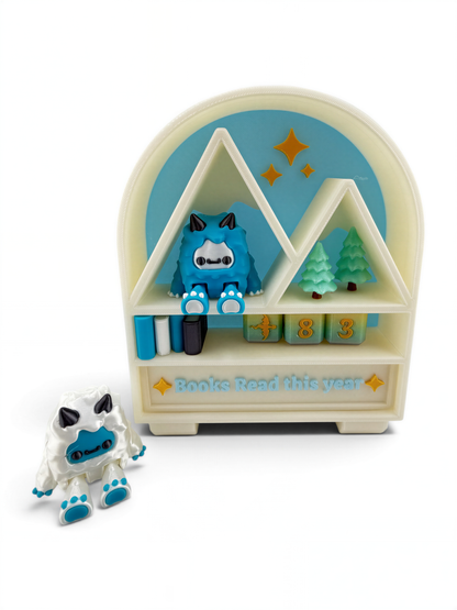 A toy shelf with a blue and white monster figurine and a toy tree on it, along with a sign that says "Books Read this year".