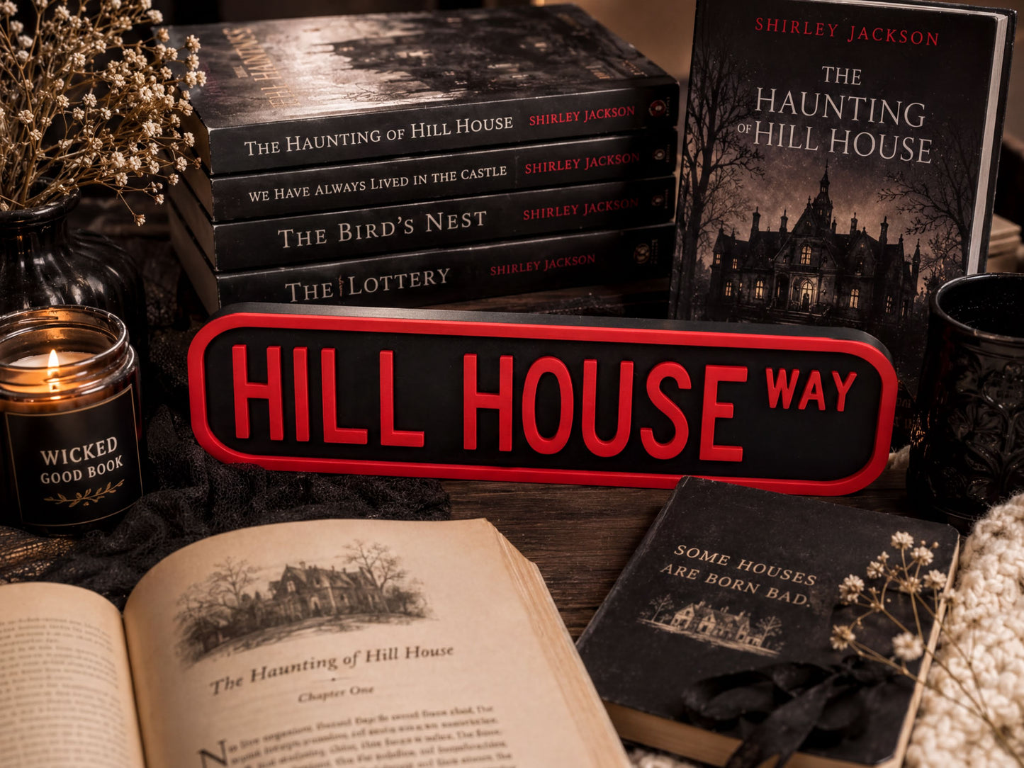 a collection of books and items related to the "Haunting of Hill House" series, including the books themselves, a candle, and a sign with the title "HILL HOUSE WAY".