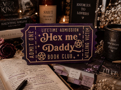 a purple ticket-shaped object with text, surrounded by various books, candles, and other items, creating a cozy and mysterious atmosphere.
