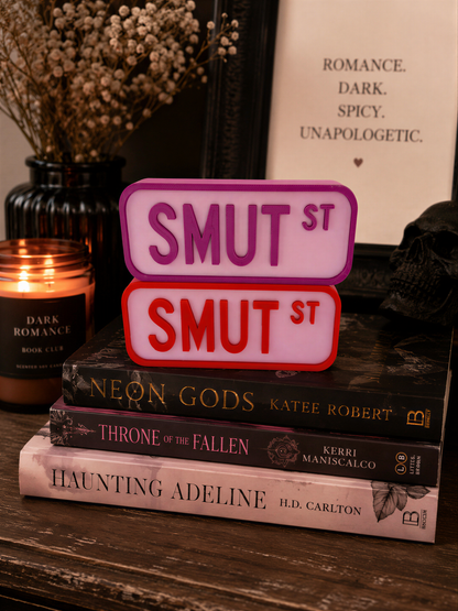a stack of books, a candle, and a framed sign with text on a wooden surface.