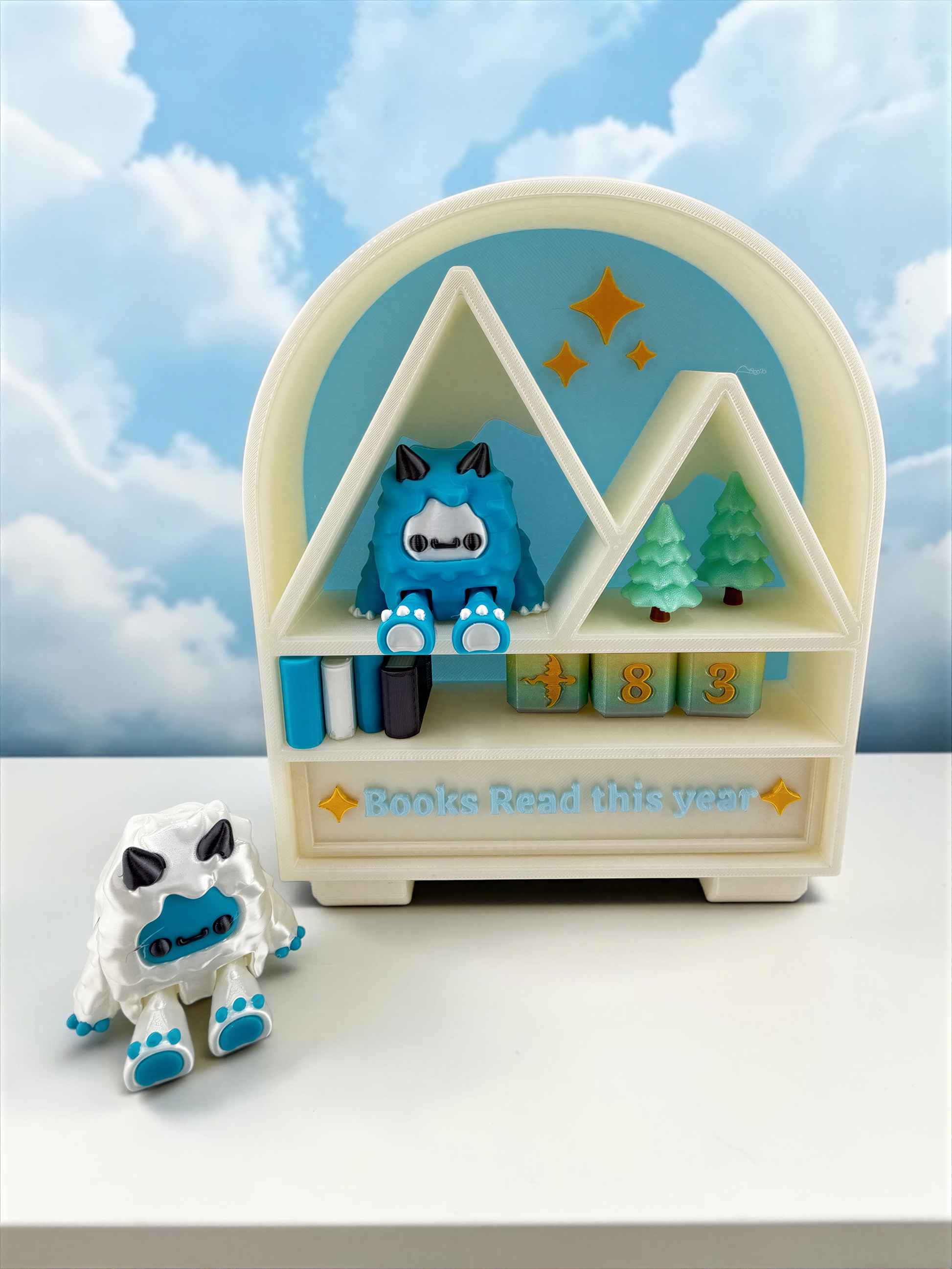 A toy shelf with a blue and white monster figurine sitting on top, and a small white toy monster figurine next to it. The shelf has a sign that says "Books Read this year".