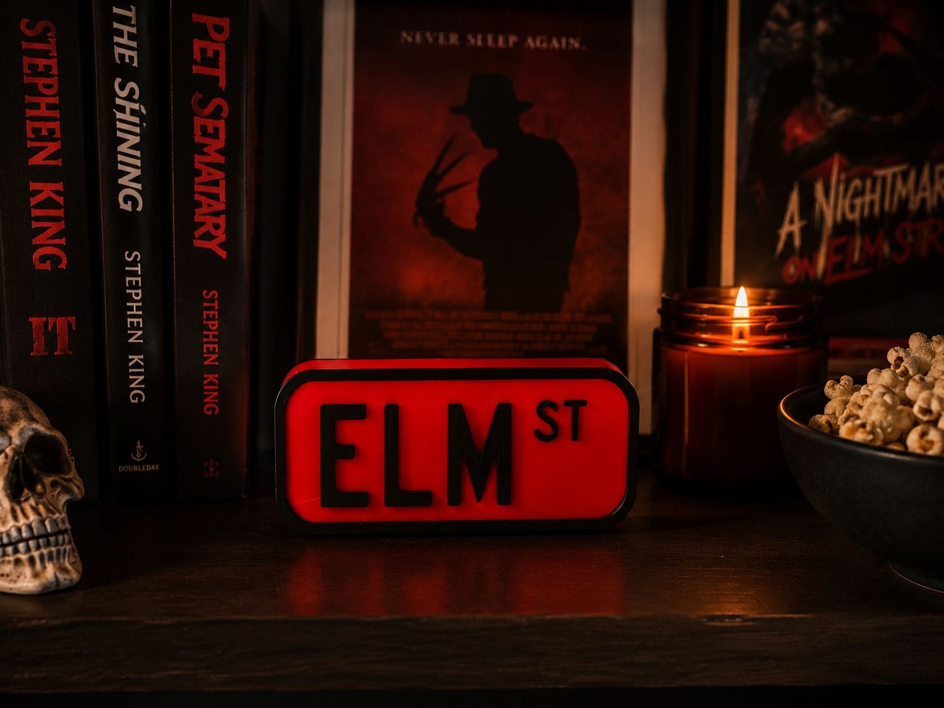 a shelf with various items, including a red and black sign that says "ELM ST", a candle, popcorn, and a skull.