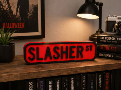 a shelf with a red sign that says "SLASHER ST" and a black lamp, surrounded by various books and a framed poster.