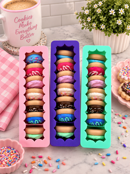 a collection of colorful donuts arranged in three different colored silicone molds, with a mug of coffee and a potted plant in the background.