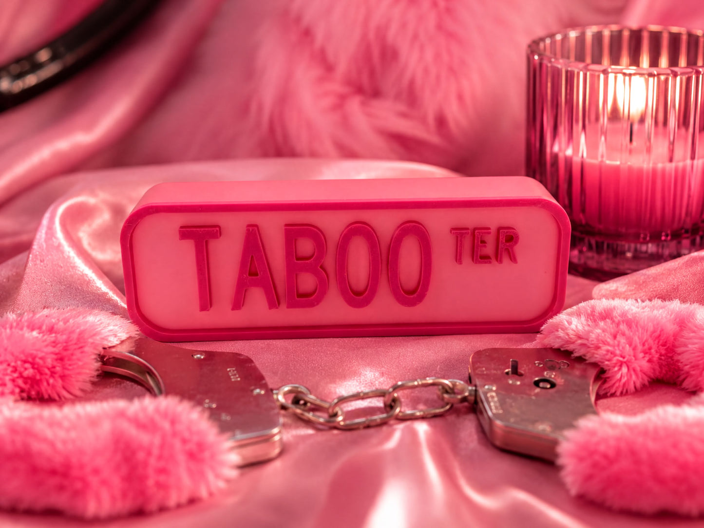 a pink Taboo sign, a pair of silver handcuffs, and a lit candle on a pink background.