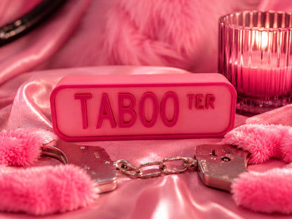 a pink Taboo sign, a pair of silver handcuffs, and a lit candle on a pink background.