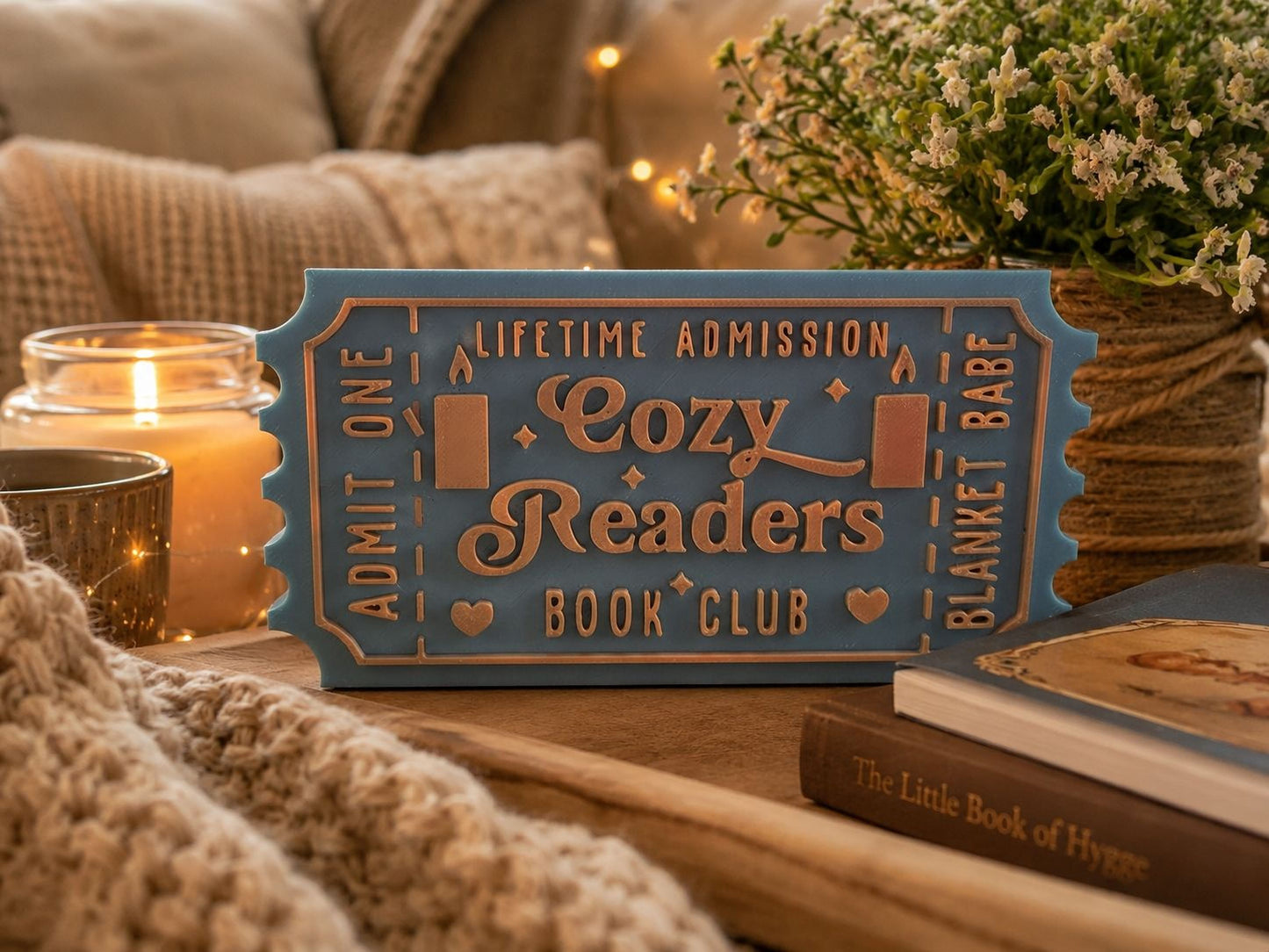 A cozy reading sign for a book club, surrounded by a candle, a potted plant, and some books, creating a warm and inviting atmosphere.