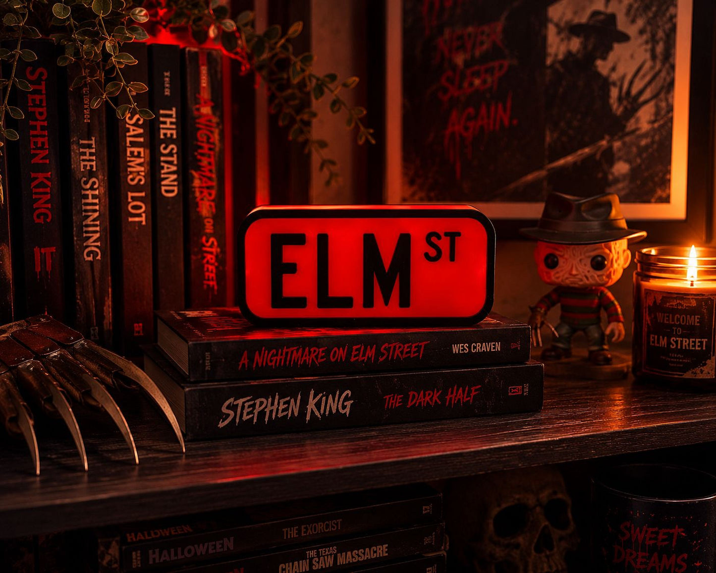 A collection of horror movie books and a figure of Stephen King's "The Dark Half" on a shelf, with a lit candle in the background.