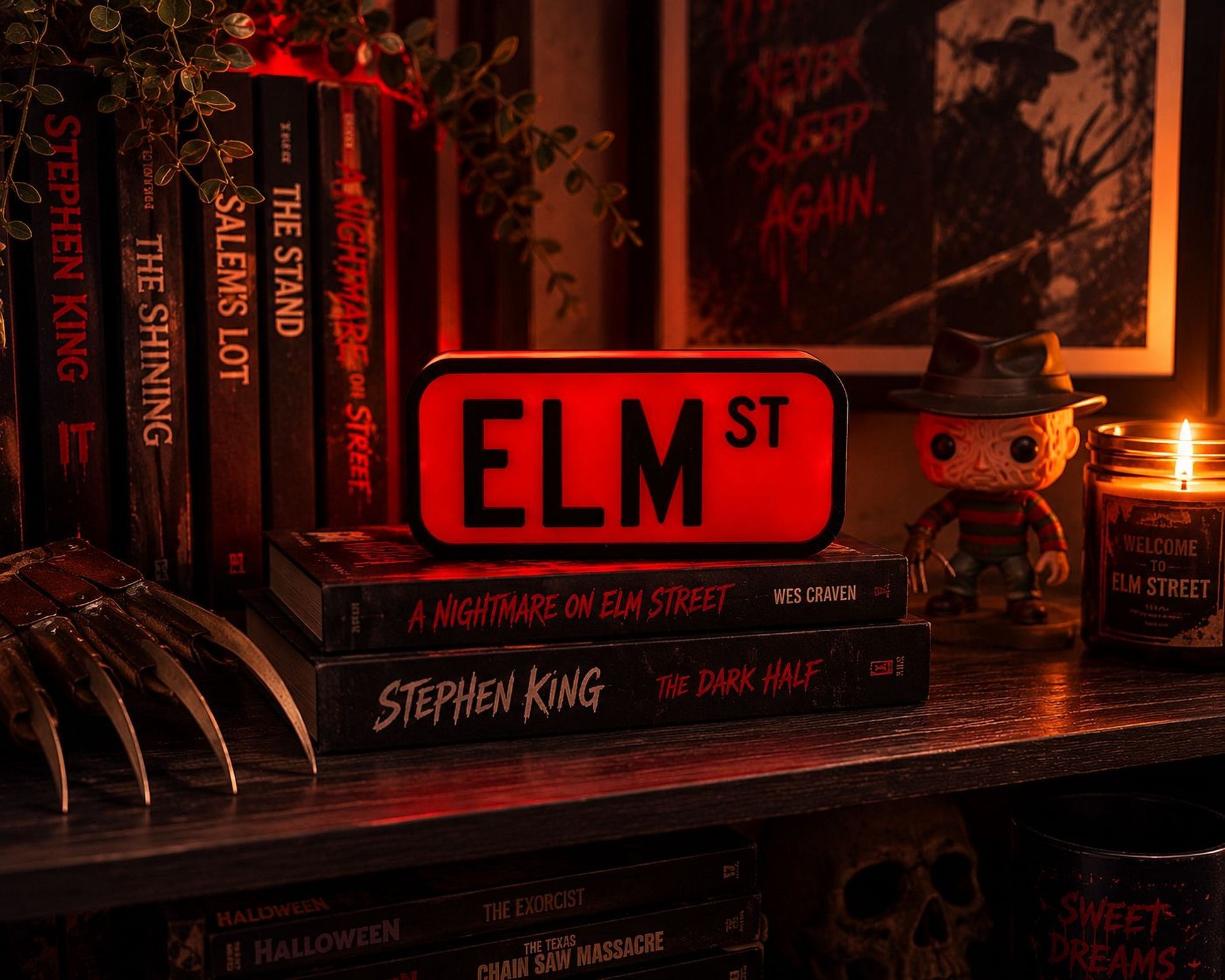 A collection of horror movie books and a figure of Stephen King's "The Dark Half" on a shelf, with a lit candle in the background.