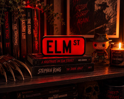 A collection of horror movie books and a figure of Stephen King's "The Dark Half" on a shelf, with a lit candle in the background.