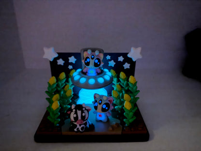 A whimsical display featuring three small, glowing animal figurines in a nighttime setting, surrounded by plants and stars.