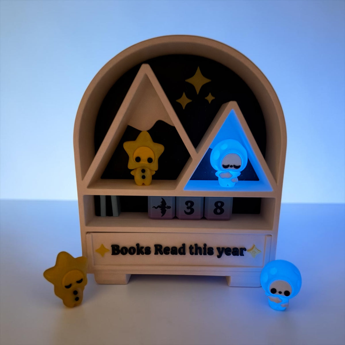 A wooden bookshelf with a sign that says "Books Read this year" and three small figurines on the shelf.