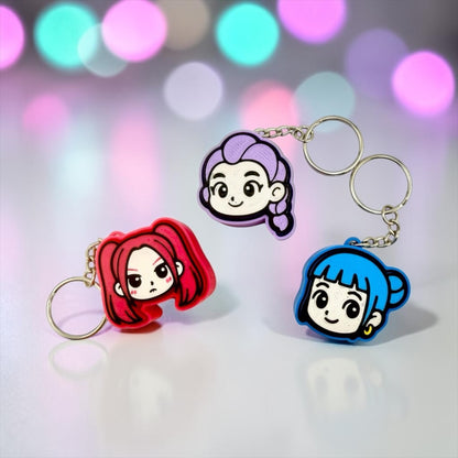 three keychains with cartoon-style faces on them, set against a background with colorful bokeh lights.