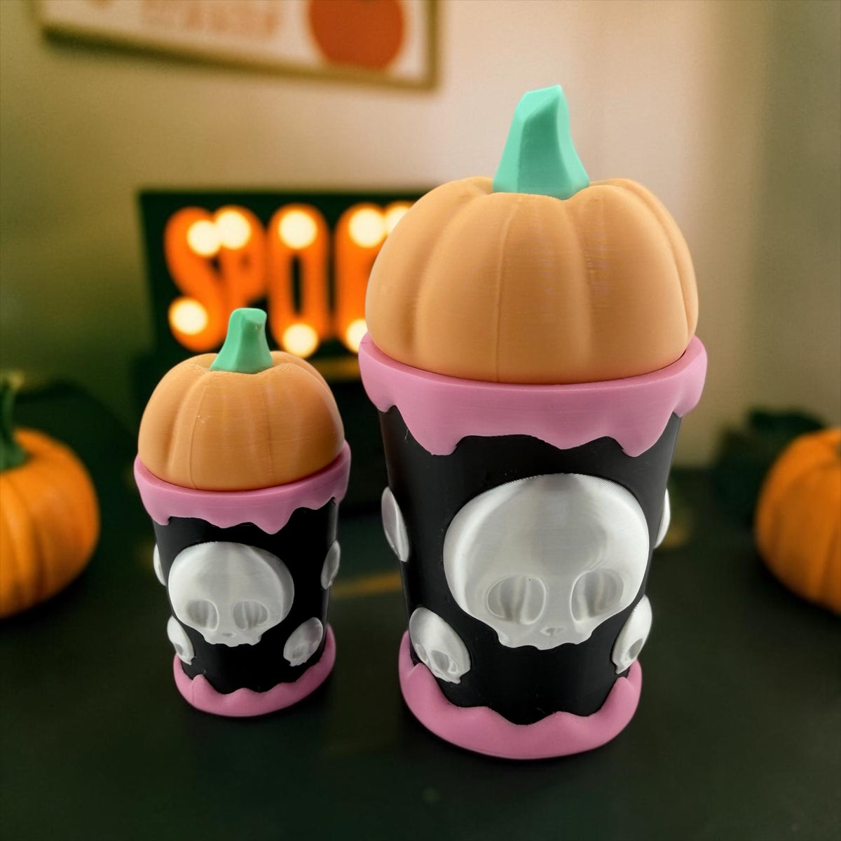 two small, colorful Halloween-themed cups with skull designs on them, placed on a table with two small pumpkins in the background.