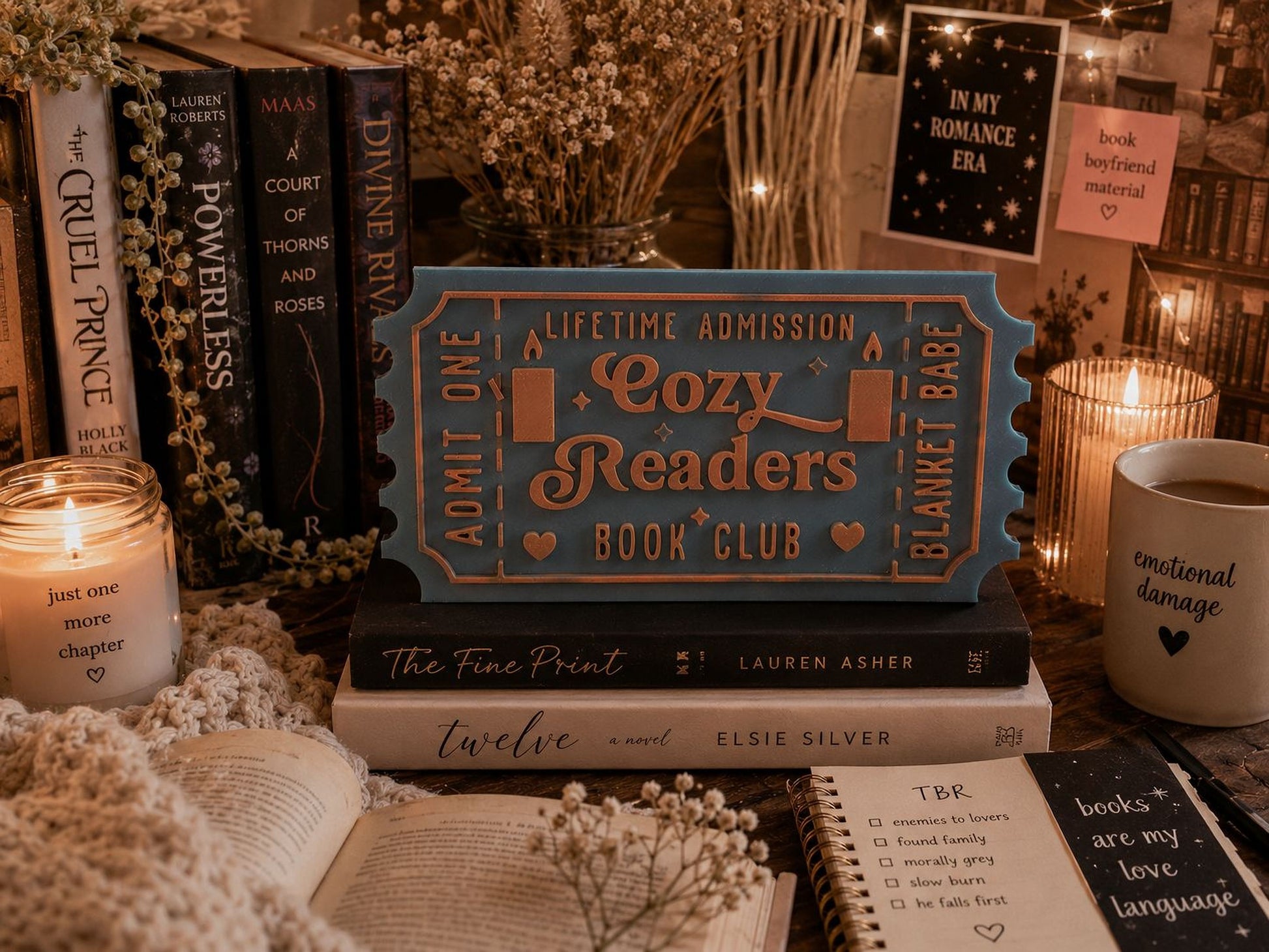 a cozy reading nook with various books, a candle, and a ticket for a book club.
