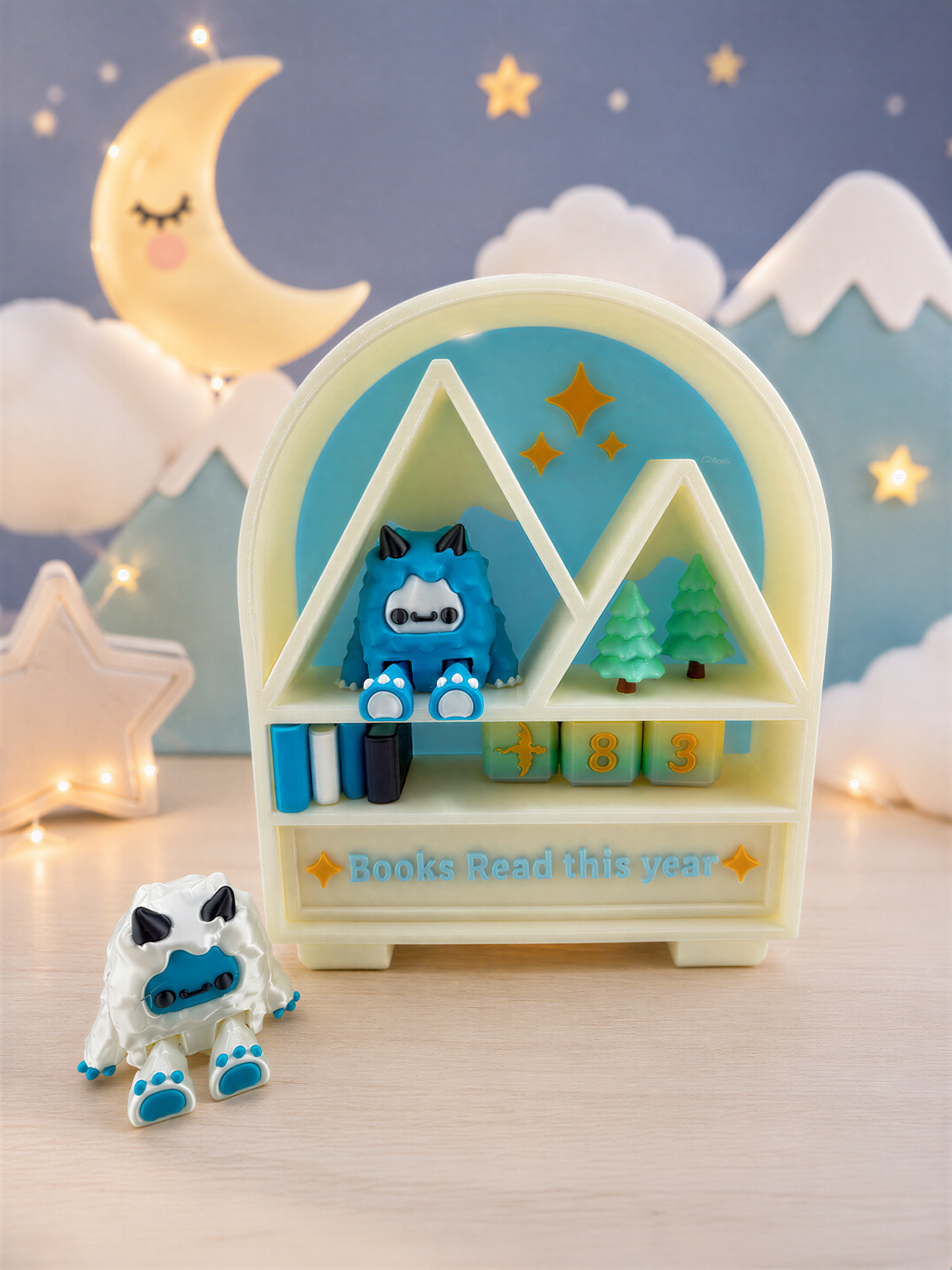 A toy shelf with a blue monster figurine and a white monster figurine, along with a sign that says "Books Read this year". The shelf is set against a night sky background with a crescent moon and stars.