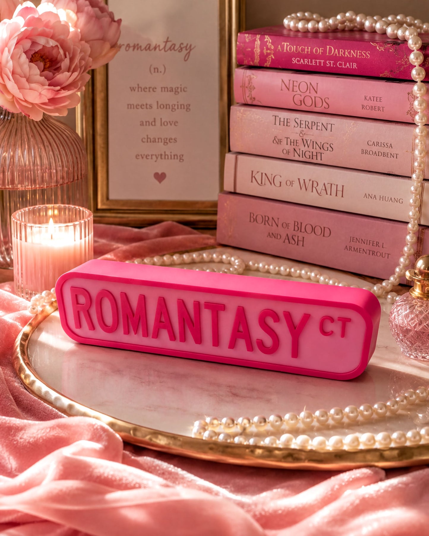 a pink object with the word "ROMANTASY" on it, surrounded by a collection of books, pearls, and a vase with flowers.