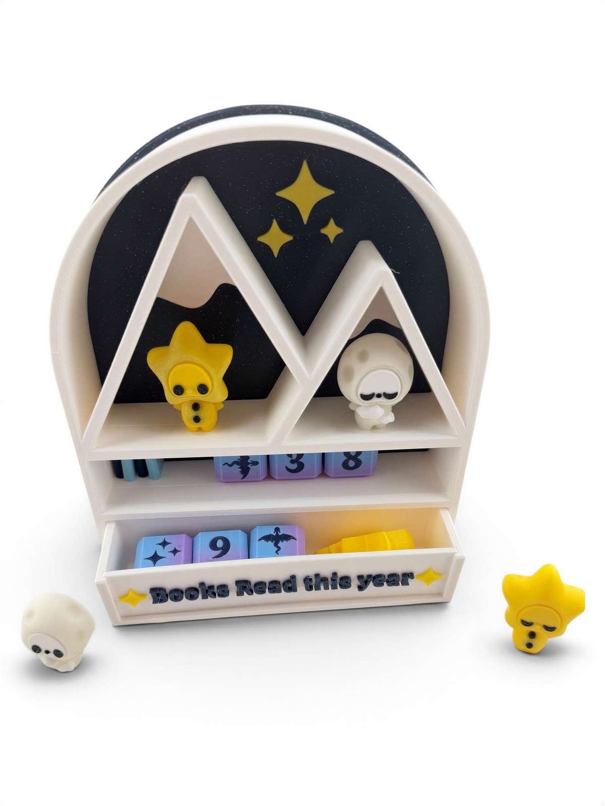A colorful toy shelf with a black and white design, featuring a yellow star and a white moon on the top shelf, and a small yellow star on the bottom shelf. The shelf also has a sign that says "Books Read this year".