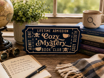 a desk with various items, including a book titled "The Cat Who Knew Too Much", a mug, a potted plant, a pair of glasses, a notebook, and a sign that says "Lifetime Admission Cozy Mystery Book Club".