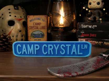 a sign that reads "CAMP CRYSTAL LN", surrounded by various Halloween-themed items such as a mask, a lantern, and books.