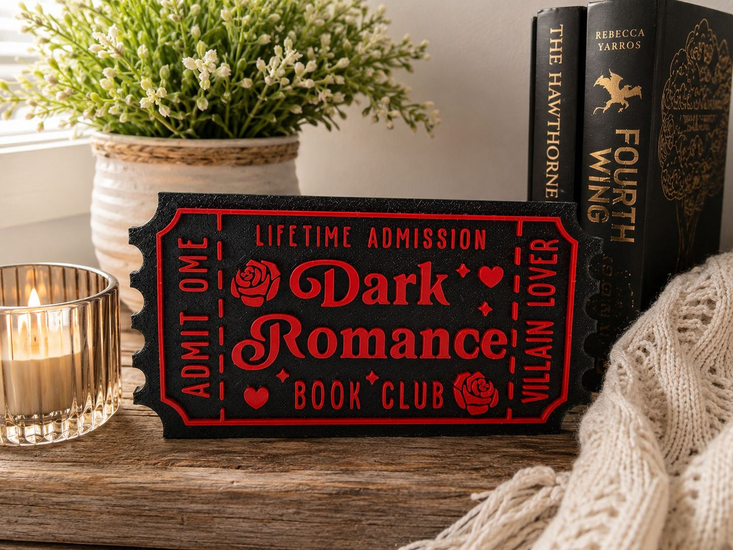 a book-themed scene with a book-shaped ticket, a candle, and some books on a wooden surface.
