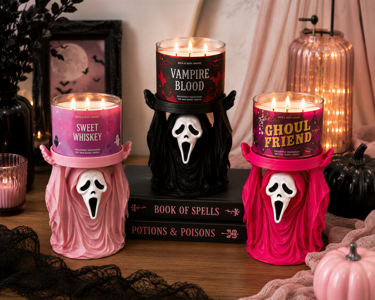 three Halloween-themed candles with spooky faces, placed on a wooden surface. The candles are labeled "Vampire Blood", "Sweet Whiskey", and "Ghoul Friend". There are also some books and decorative items in the background, creating a festive atmosphere.