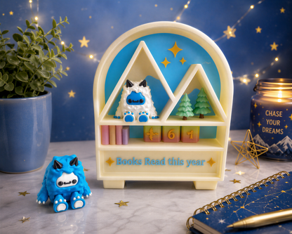 a whimsical scene with a toy shelf displaying a blue monster, a small blue monster figurine, and a toy castle. The shelf also has a sign that says "Books Read this year". The shelf is set against a starry night sky background, and there are some potted plants and a candle in the scene.