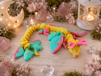 A colorful dragon figurine made of play-doh is displayed on a wooden surface, surrounded by various decorative elements such as flowers, crystals, and a lantern.