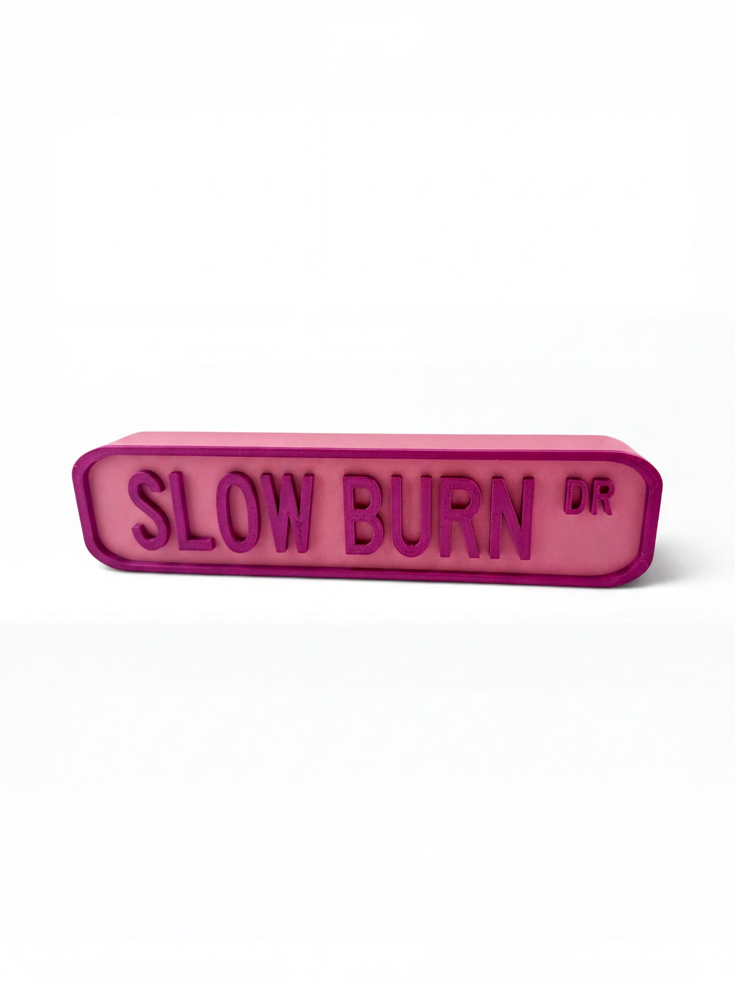 A pink rectangular sign with the text "SLOW BURN DR" in a bold, sans-serif font.