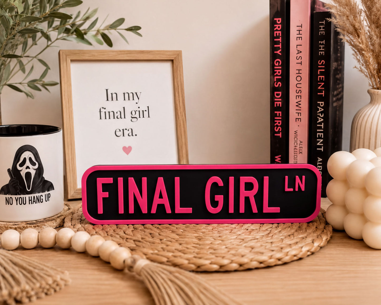 a desk with various items on it, including a framed quote, a mug with a silhouette of a person, a sign that says "FINAL GIRL", and some books.