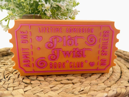 a bright orange ticket-shaped object with pink text, placed on a woven surface.