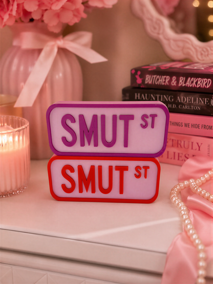 a pink vase with pink flowers, a stack of books, and a pair of red and purple license plates on a white surface.