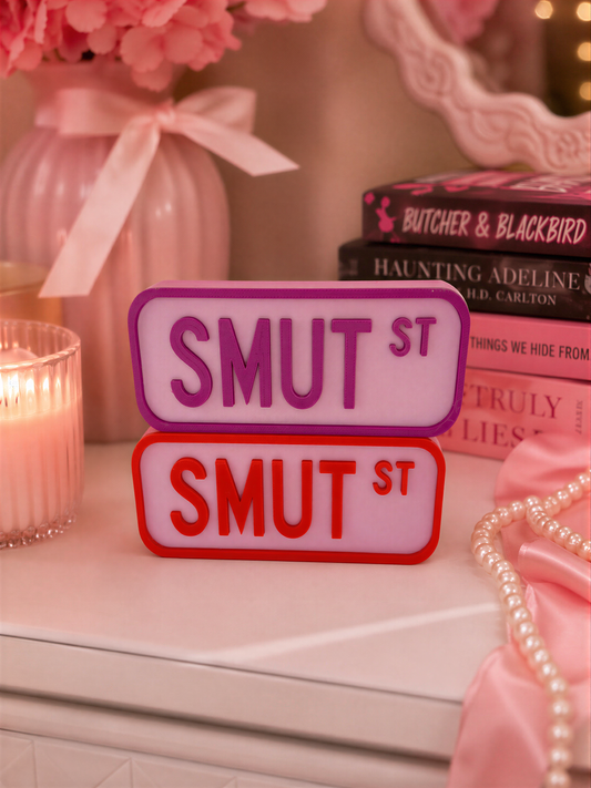 a pink vase with pink flowers, a stack of books, and a pair of red and purple license plates on a white surface.