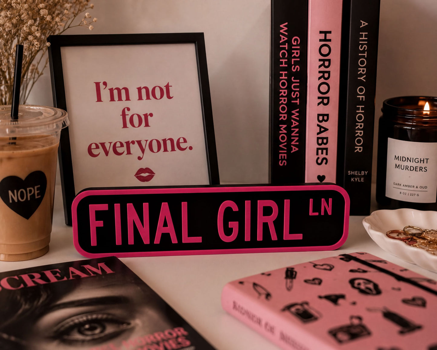 a collection of items related to the "Final Girl" movie franchise, including a framed quote, a pink sign, a candle, and various books and magazines.