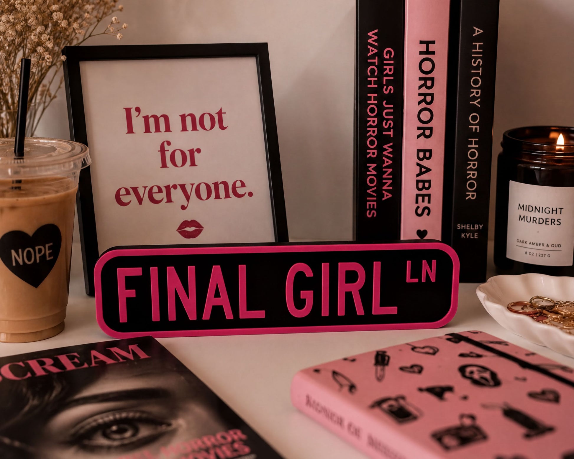 a collection of items related to the "Final Girl" movie franchise, including a framed quote, a pink sign, a candle, and various books and magazines.