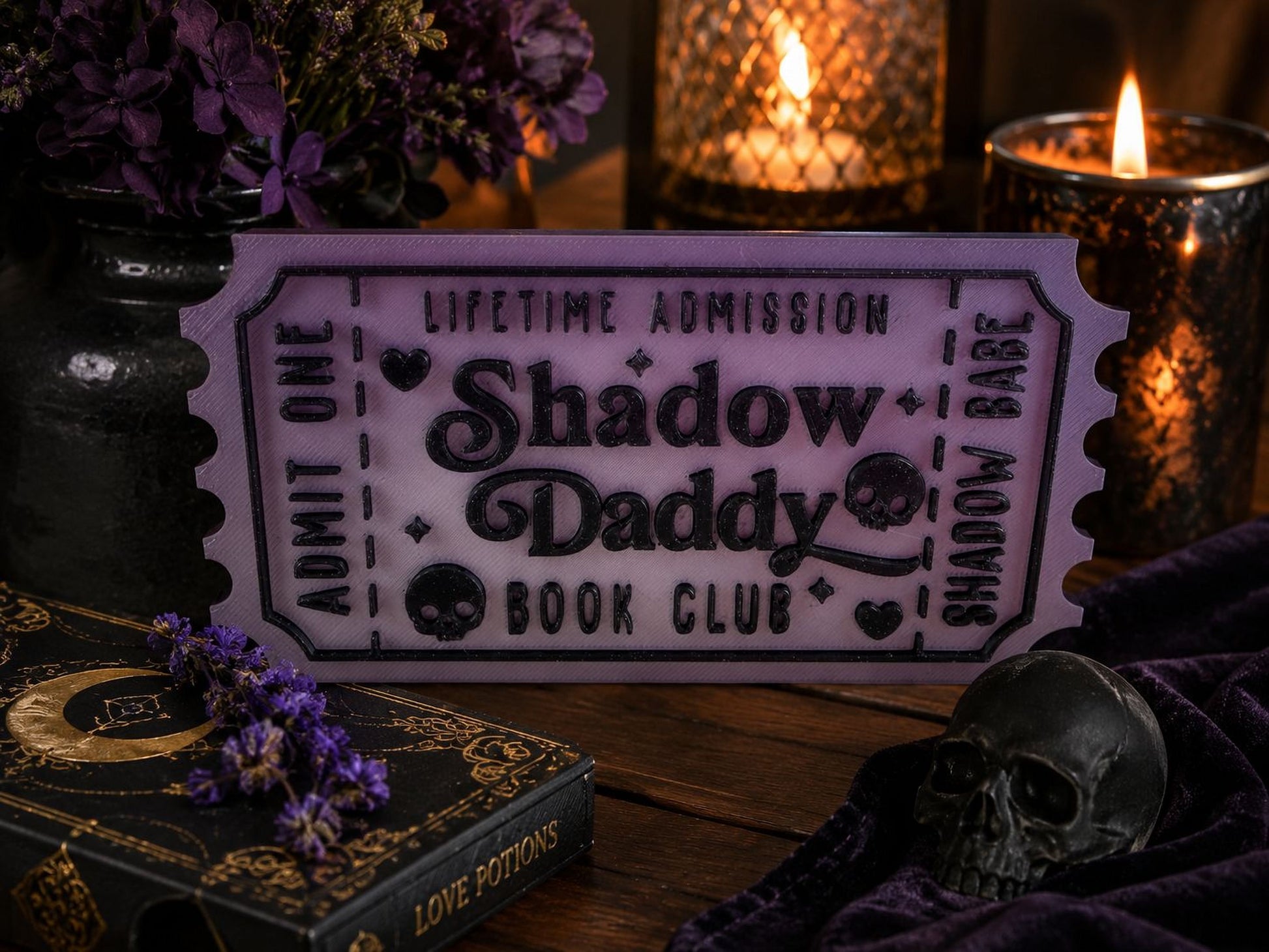 a purple ticket-shaped sign with the text "Lifetime Admission Shadow Daddy Book Club" on it, surrounded by various objects such as a candle, a skull, and a book.
