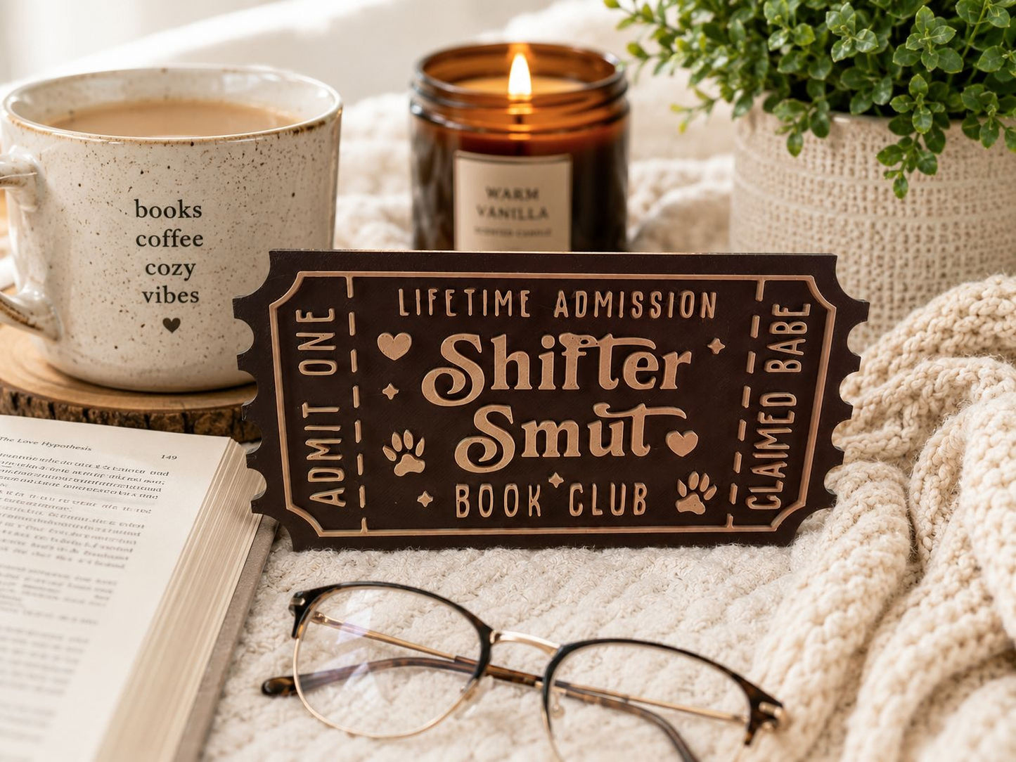a cozy scene with a book, a pair of glasses, a candle, and a ticket for a book club.