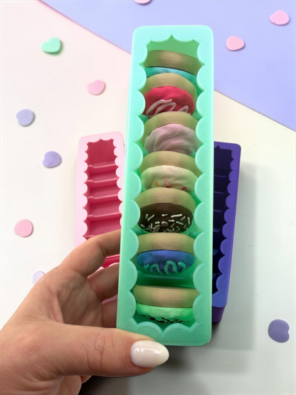 A hand holding a green container filled with colorful donuts, with a background of confetti.