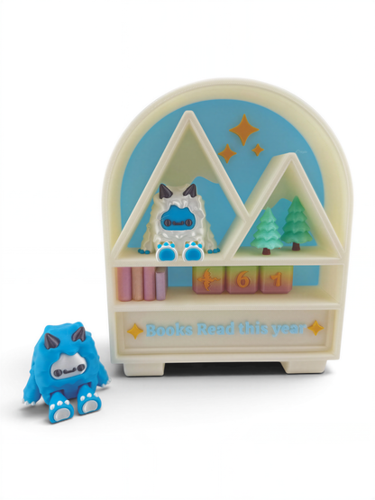 A toy shelf with a blue monster figurine sitting on it, and a small blue monster figurine next to it. The shelf has a sign that says "Books Read this year".
