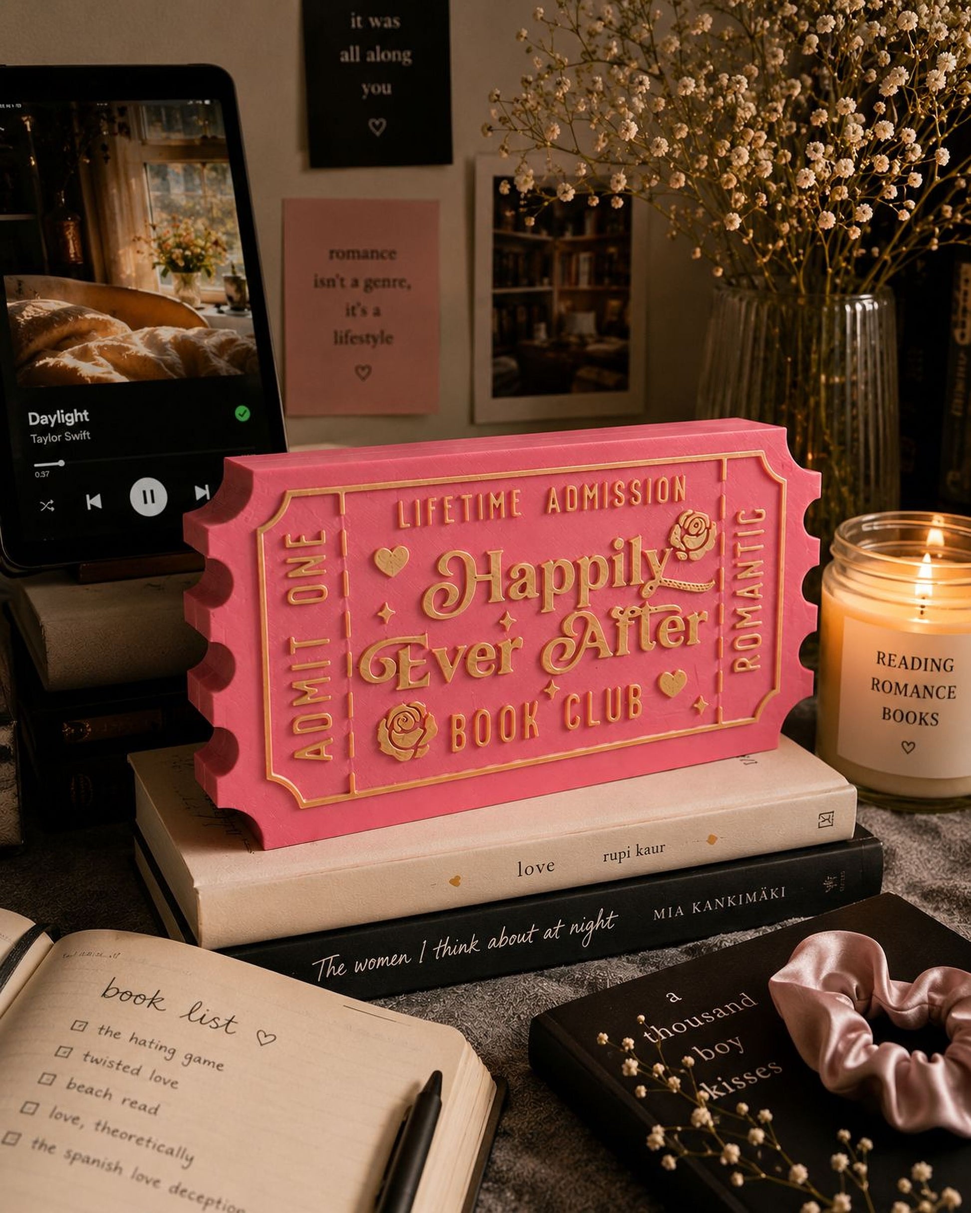 a pink ticket-shaped object with text, surrounded by various items such as a candle, books, and a notebook.