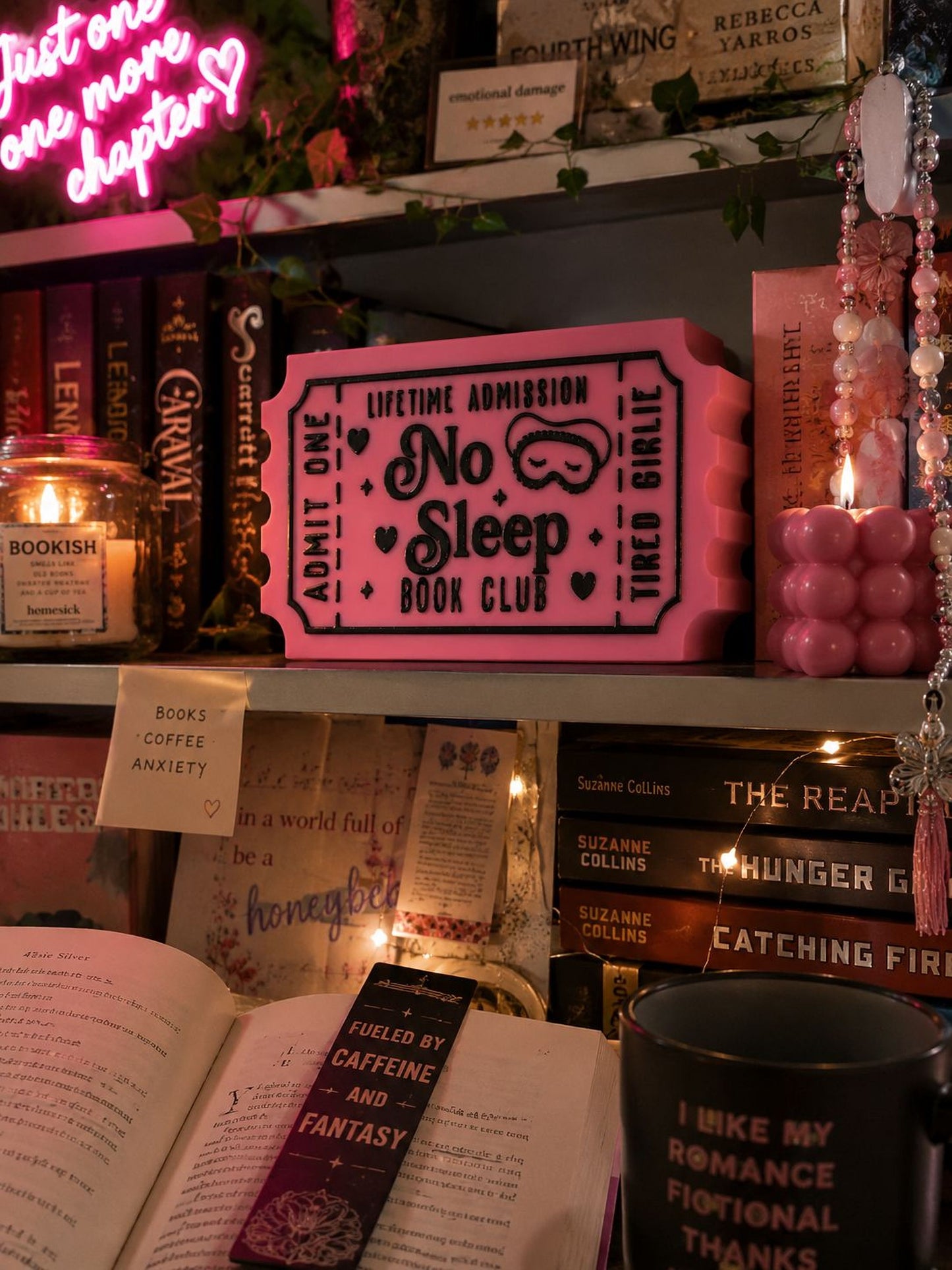 a bookshelf filled with various books, a pink ticket-shaped sign, and a black mug with text on it. The bookshelf is decorated with pink and white lights, and there are other items such as a candle, a plant, and a necklace.