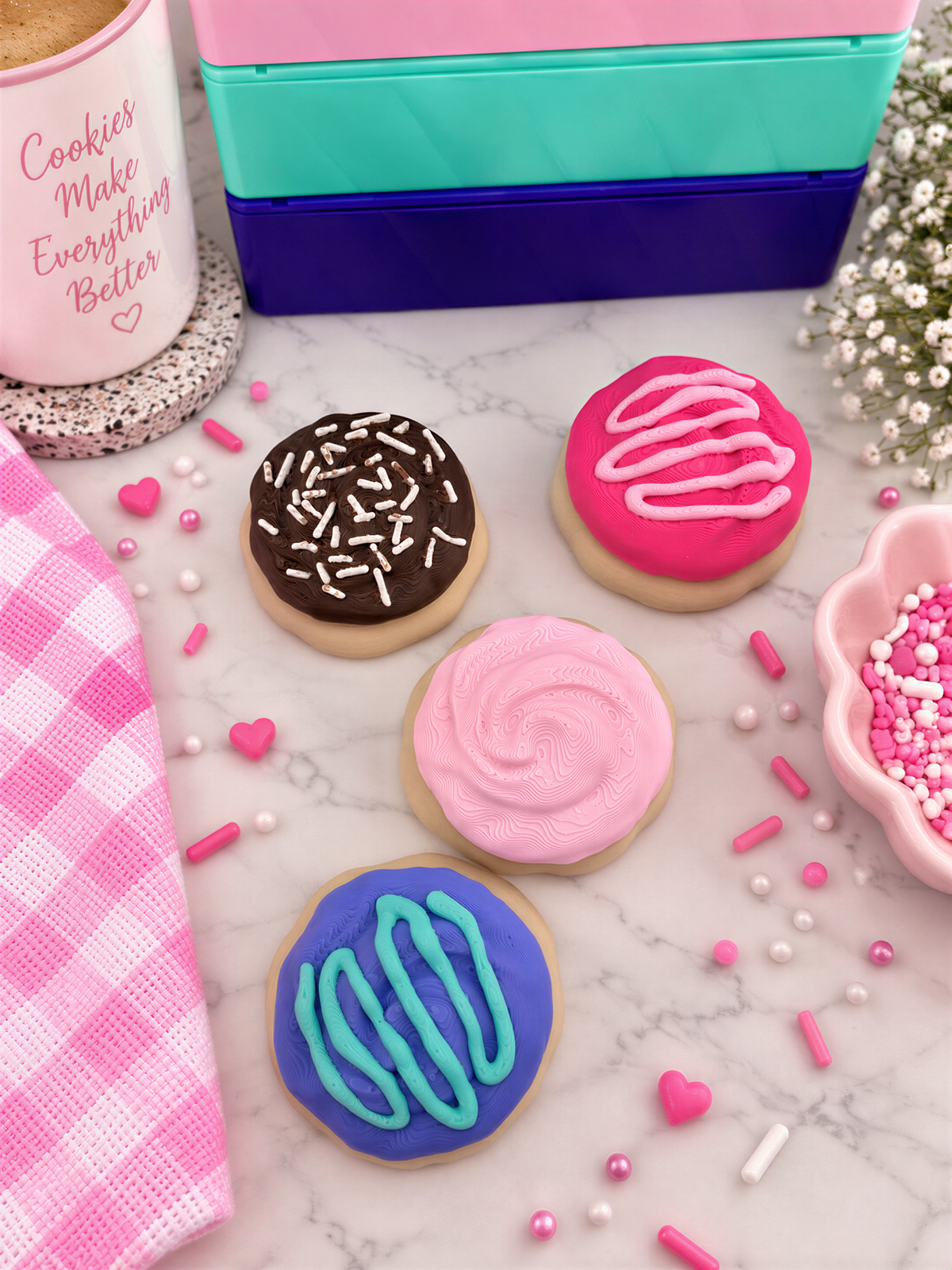 a variety of colorful and decorated cookies, including chocolate, pink, blue, and white frosted cookies, as well as sprinkles and a pink cup.