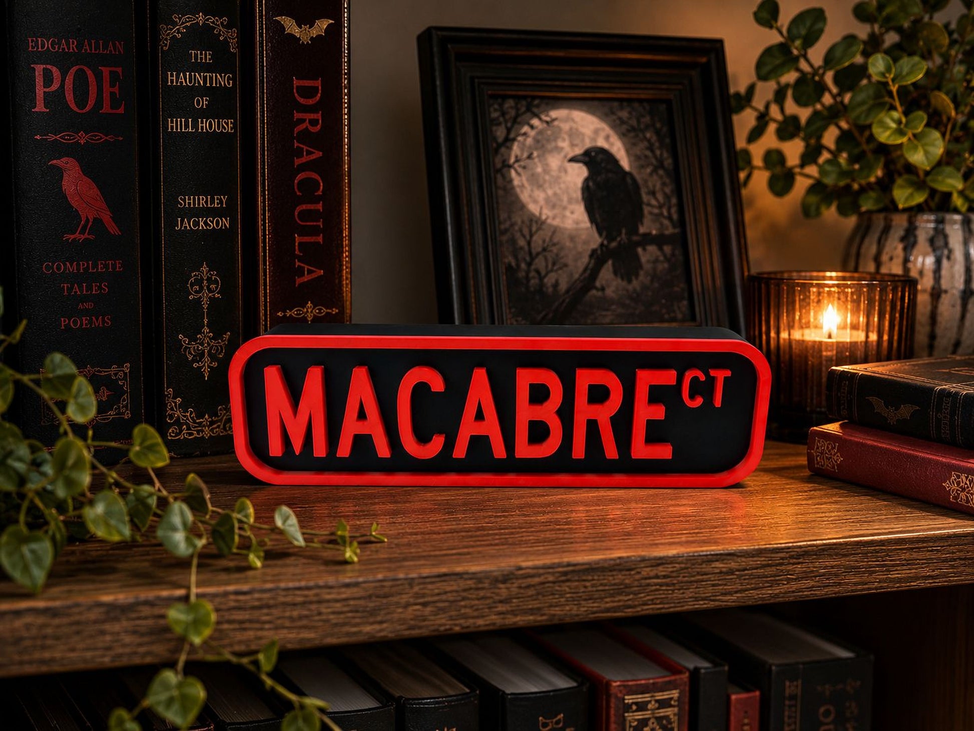 a bookshelf with various books, a framed image of a black bird, and a red sign with the word "MACABRE" on it. There is also a candle and some greenery in the background.