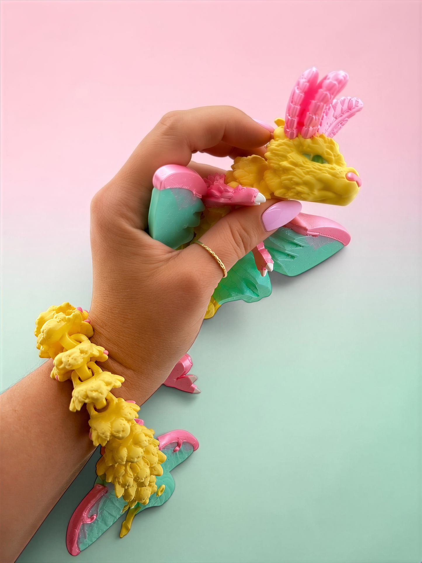 A hand is holding a colorful toy in a pink and green color scheme against a pink and green background.