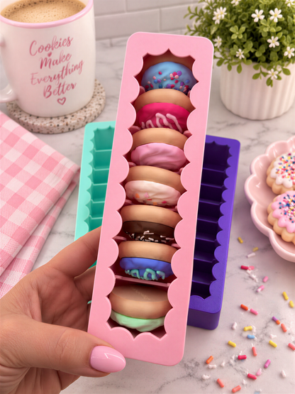 A hand holding a pink container filled with colorful donut-shaped cookies, surrounded by other donut-shaped cookies and a mug with the text "Cookies Make Everything Better".