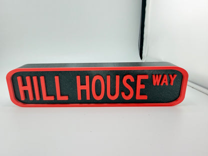 A red and black rectangular sign with the text "HILL HOUSE WAY" on it.